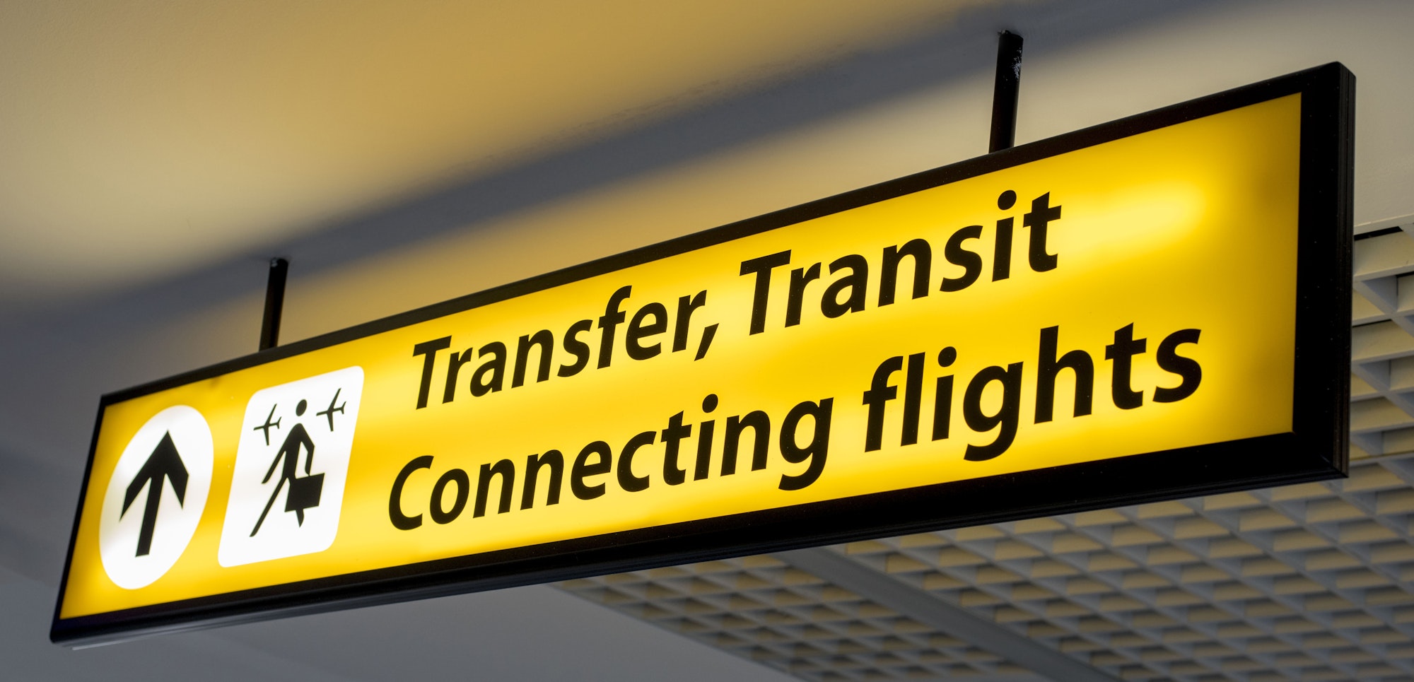 Yellow and black "Transfer, Transit, Connecting flights" information board sign at airport